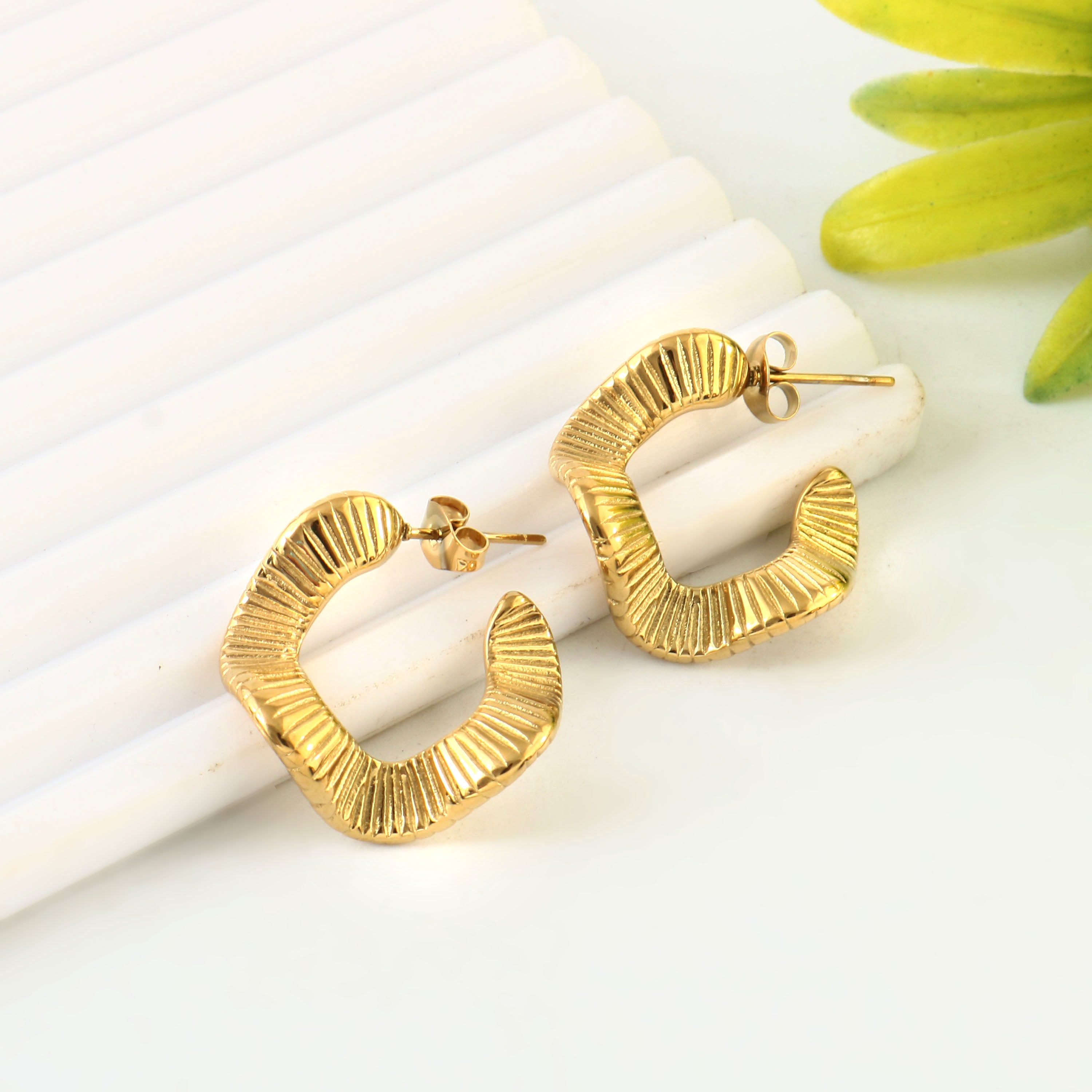 Gold hoop earrings on a white surface with a green flower in the background